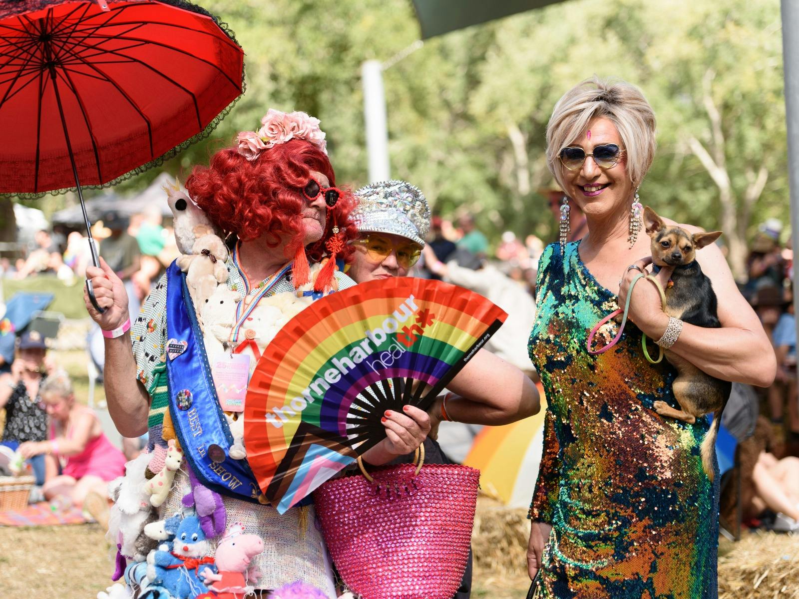 A drag queen holds a Rainbow Thorne Harbour health fan, their dress is covered in soft toys