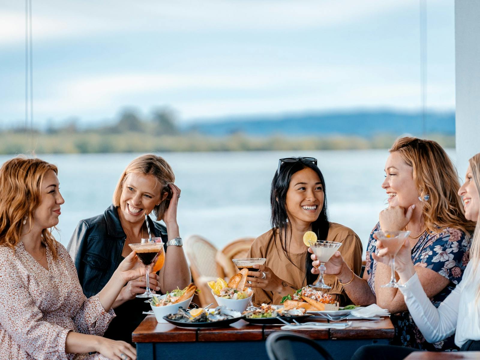 4 women having cocktails by the river