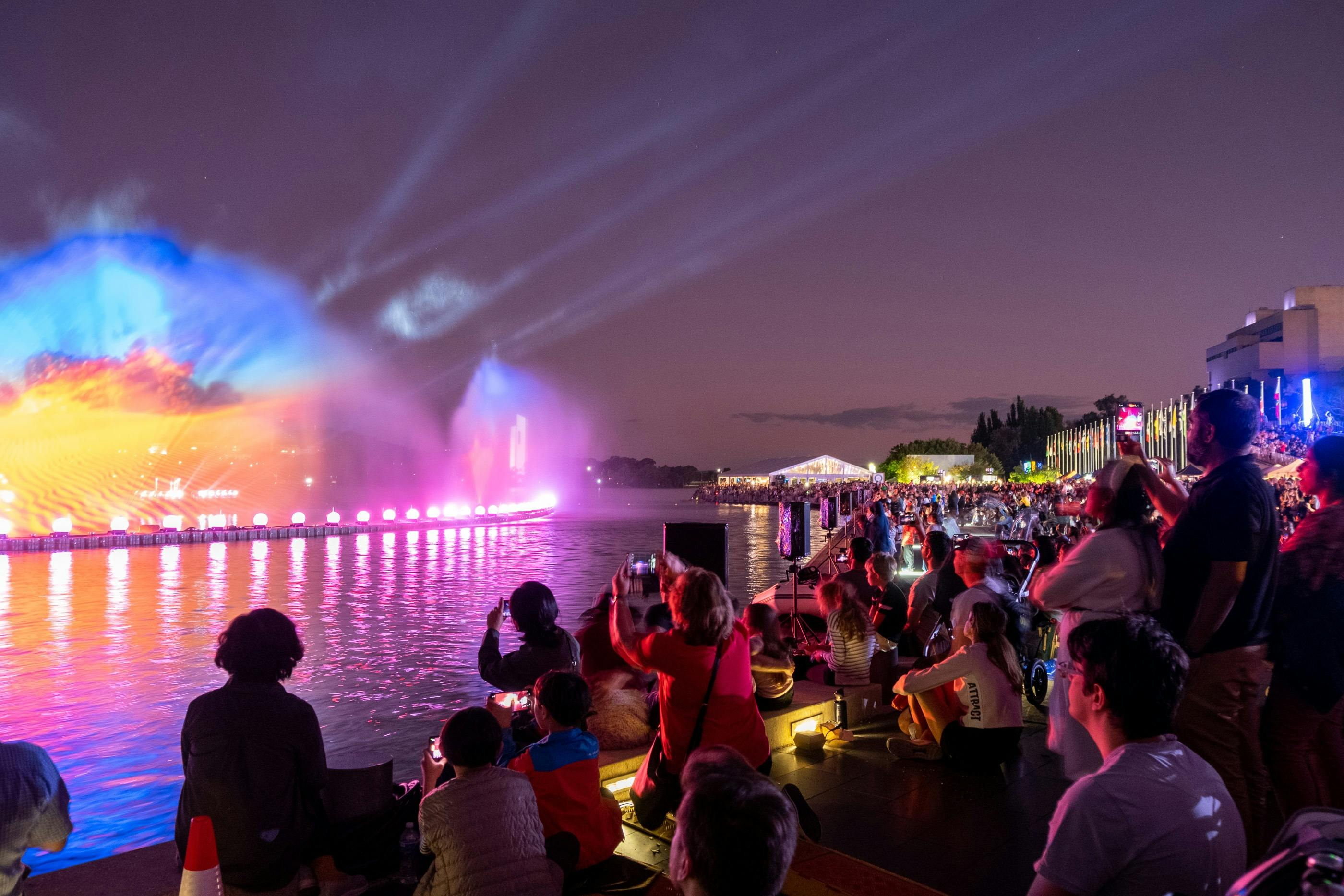 People gather aroudn a light display on Lake Burley Griffin