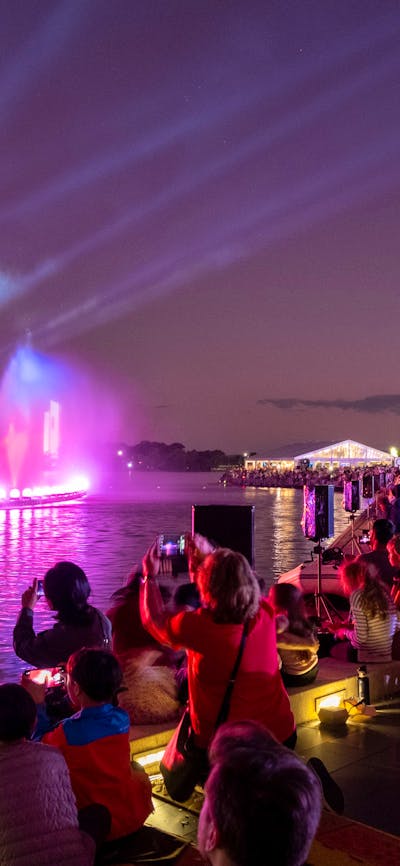 People gather aroudn a light display on Lake Burley Griffin