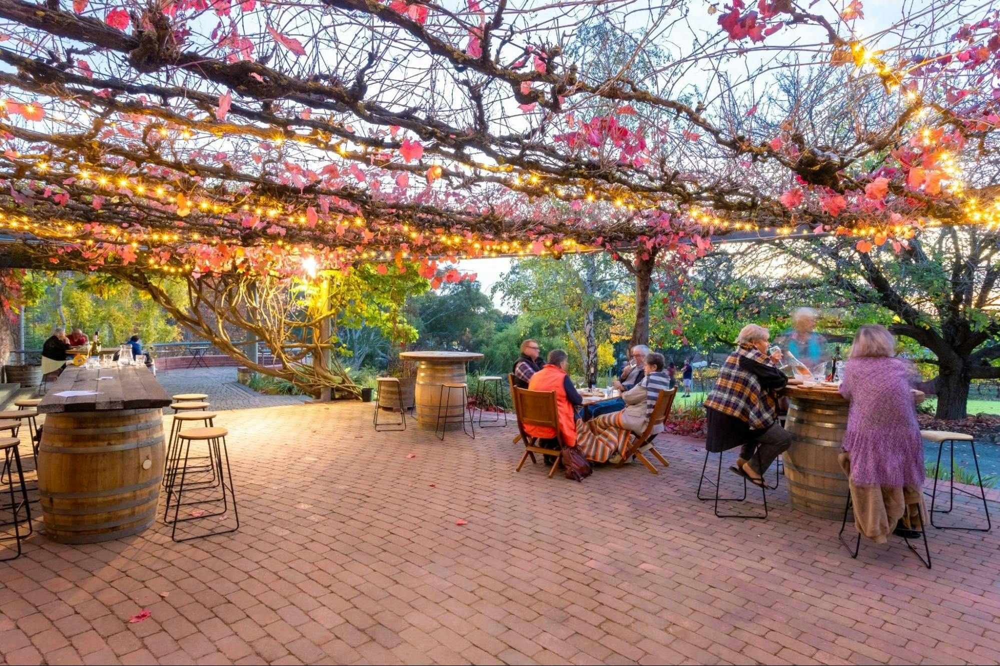Group sitting around a barrell on a terrace at dusk lit by fairy lights