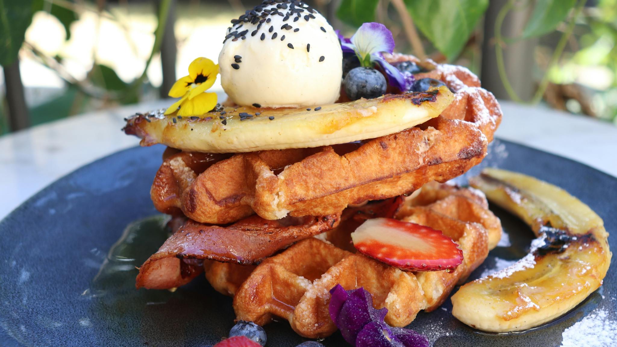 A stack of two waffles topped with a scoop of vanilla icecream, berries, banana and maple syrup.