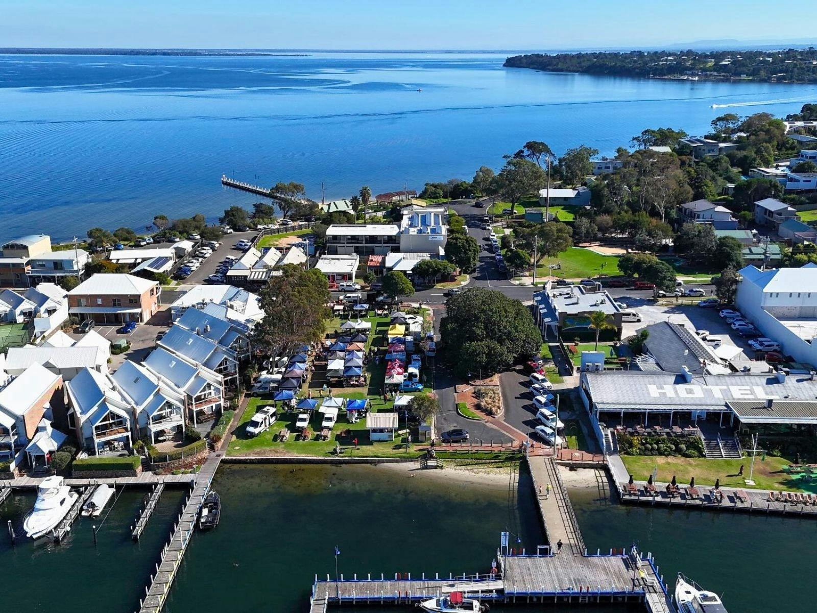 Aerial view looking down at Metung Market with stalls on Metung Village Green beside Bancroft Bay