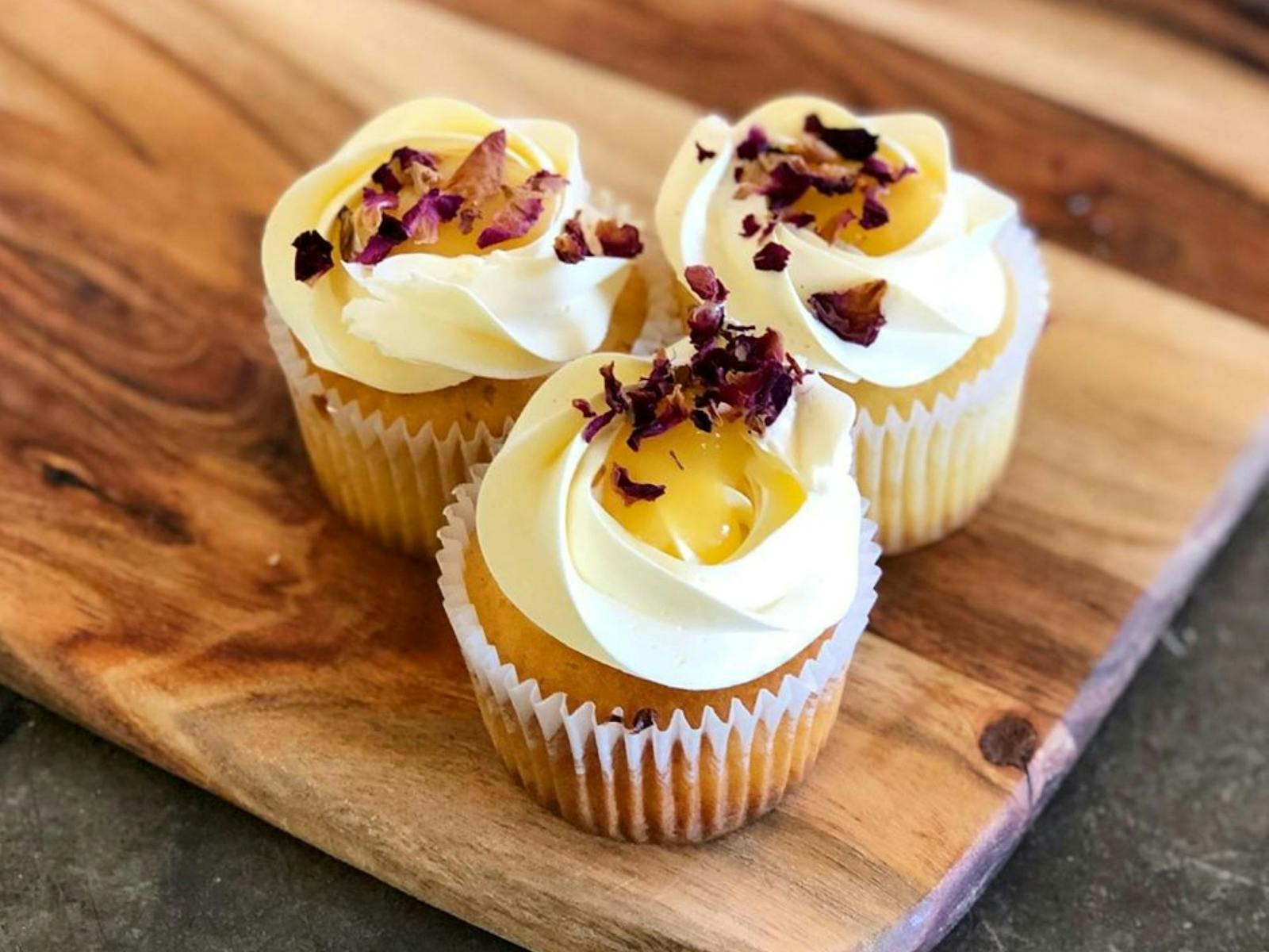 Image of three cupcakes decorated with white icing and edible flowers displayed on a chopping board