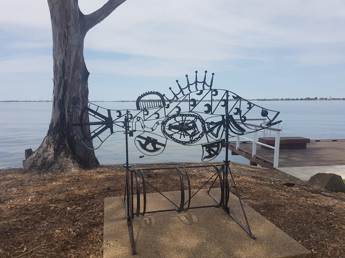 A scrap metal sculpture of a fish is silhouetted against Lake Mulwala.