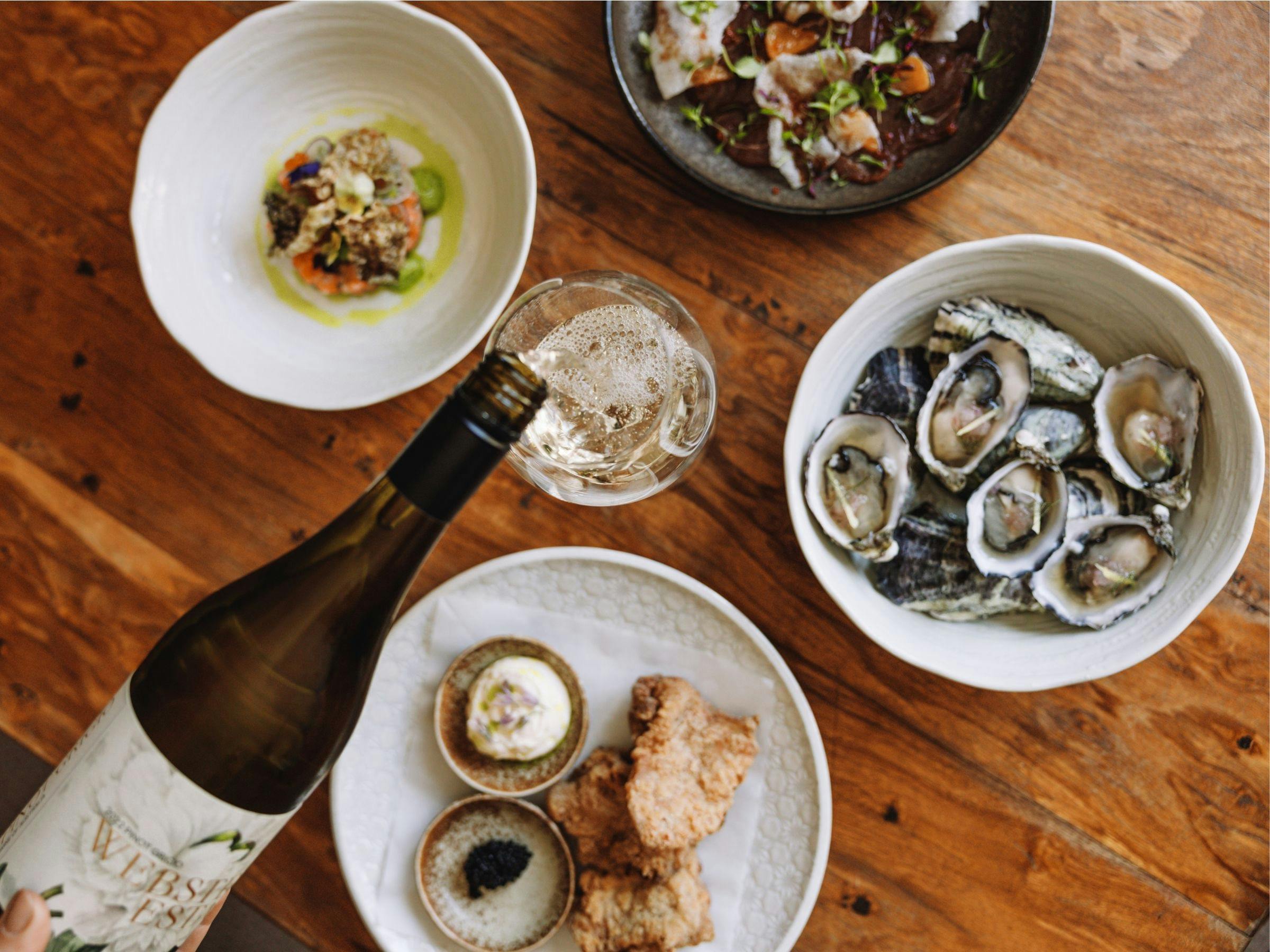 An image of food dishes spread out on the table at Elm Dining while wine is being poured