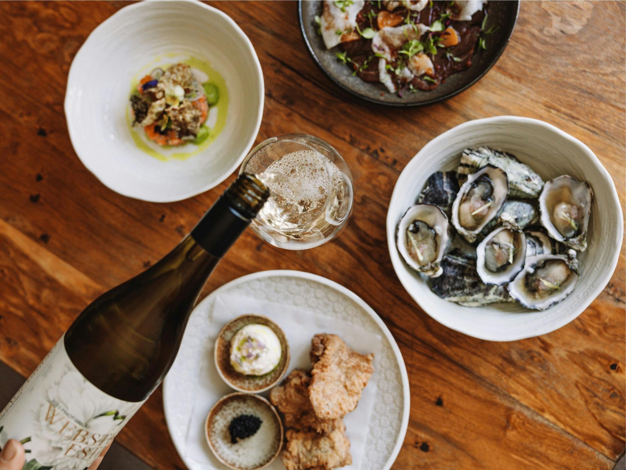 An image of food dishes spread out on the table at Elm Dining while wine is being poured