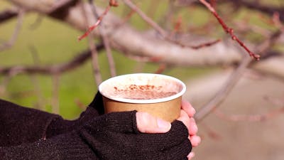 A pair of gloved hands clasp a disposable mug of hot chocolate