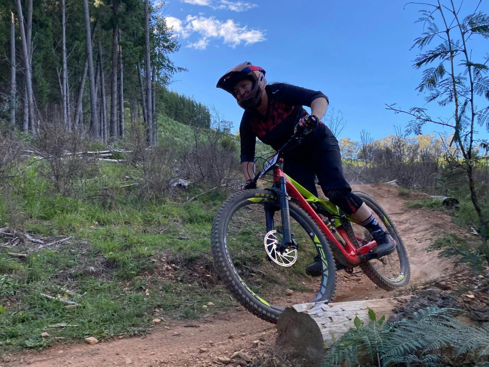 A rider wearing black rides on a dirt trail with green grass and trees in the background.