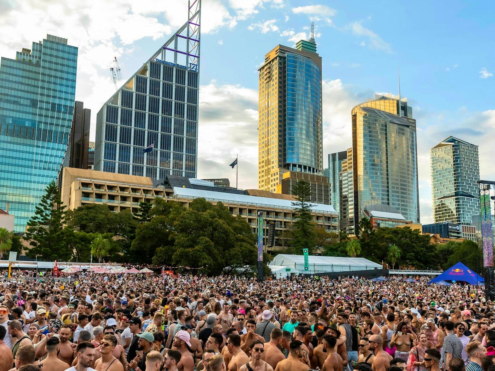 A large crowd at a music festival in front of the Sydney Skyline during sunset.
