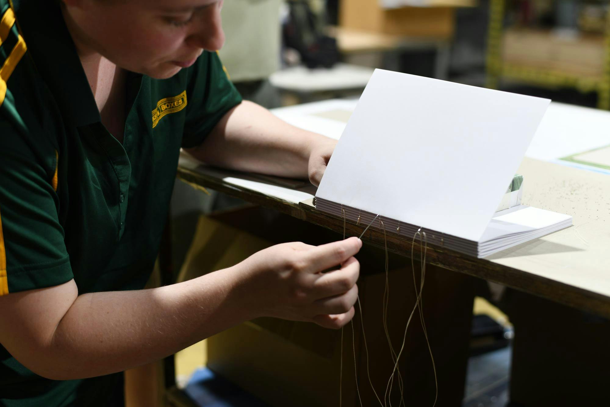 Young craftsperson operating specialist bookbinding equipment in a workshop.