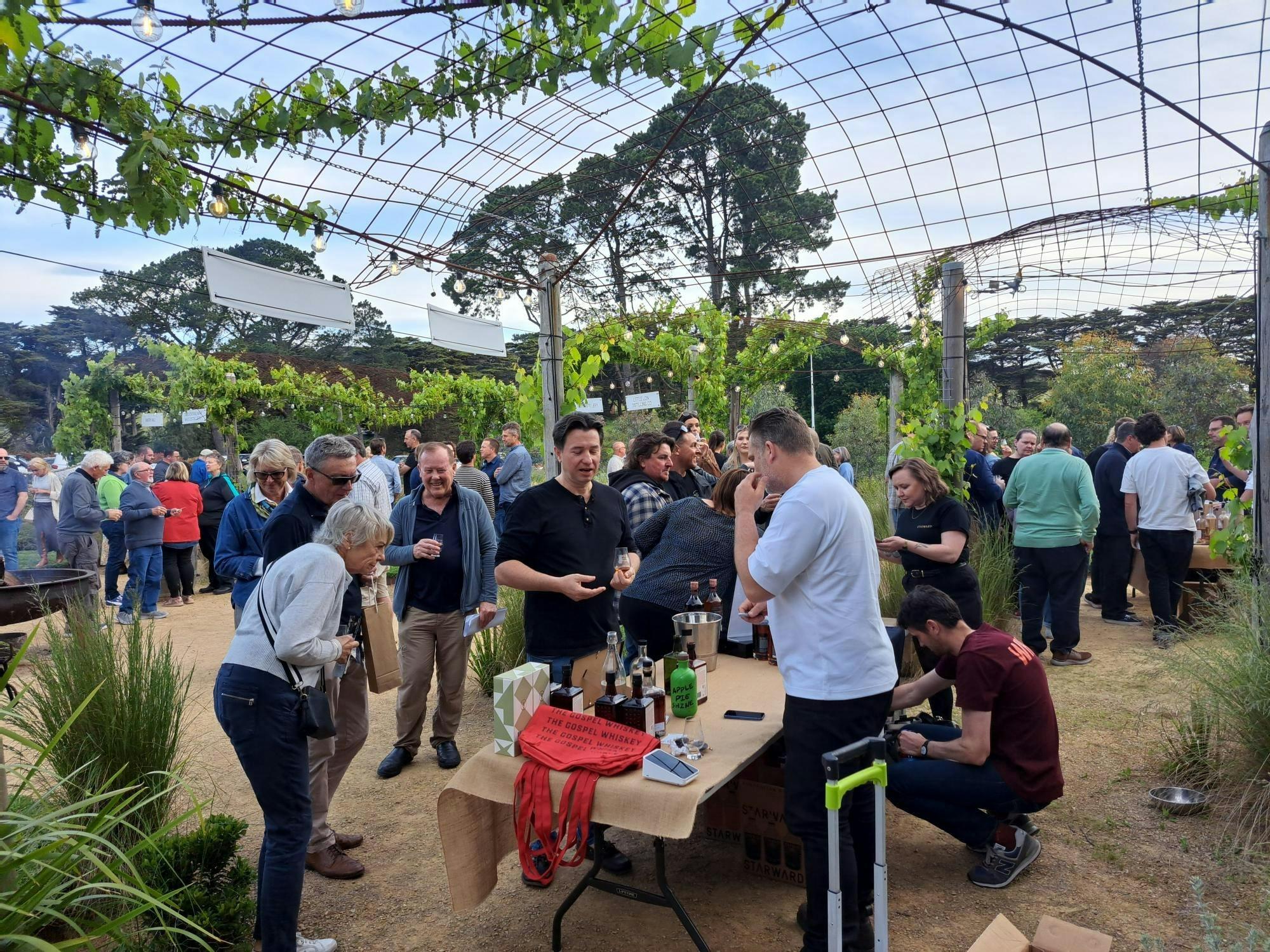 guests sampling whiskies from local distillers beneath the vine-covered pergola at The Whiskery