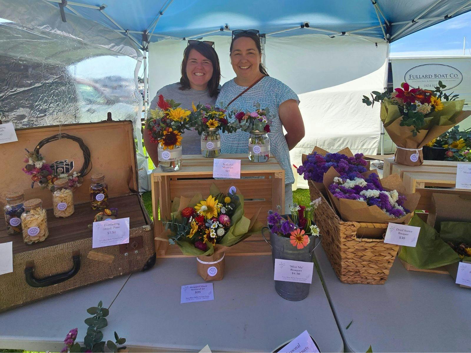 Market flower stall with bunches of flowers and two ladies standing behind table with flowers