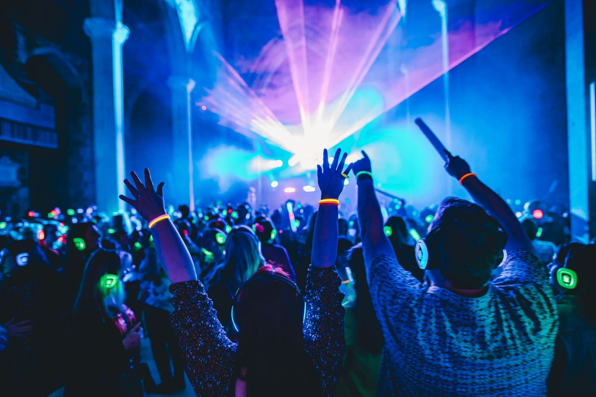 Crowd dancing to a silent disco in a hall with light show displayed above them