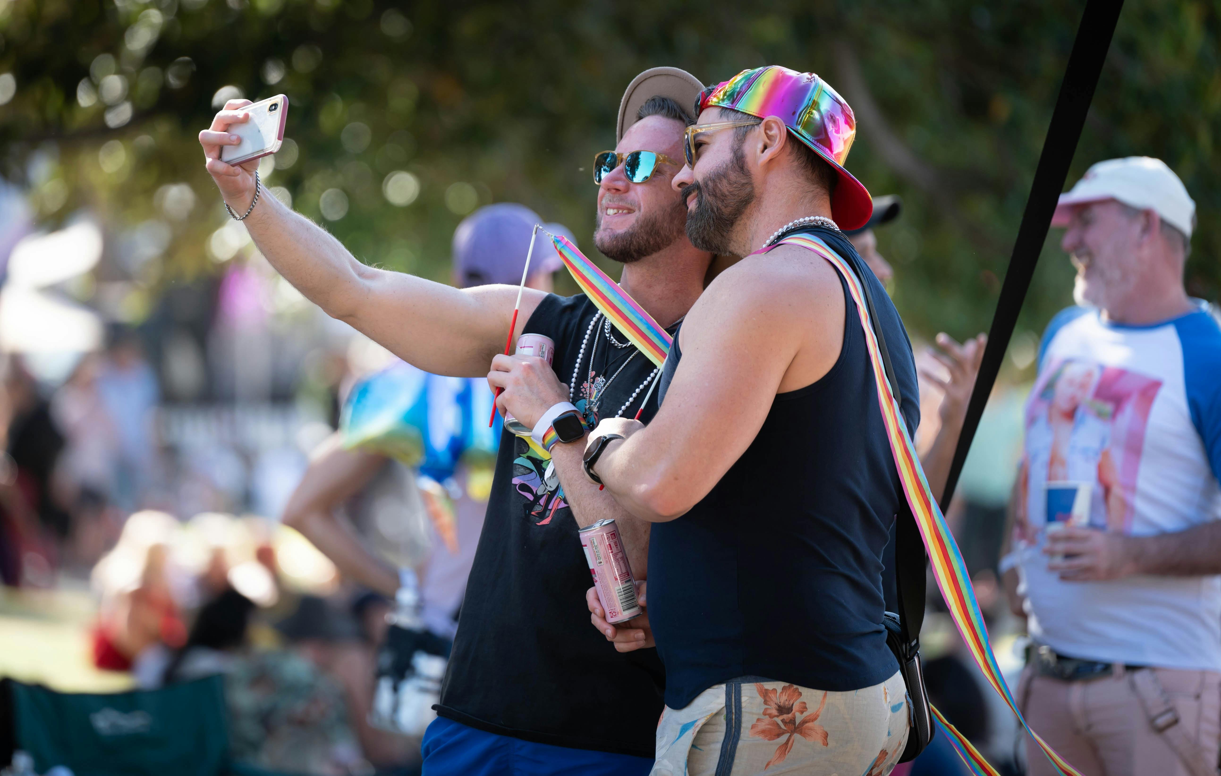"Two people in summer clothes and rainbow accessories taking a selfie together.