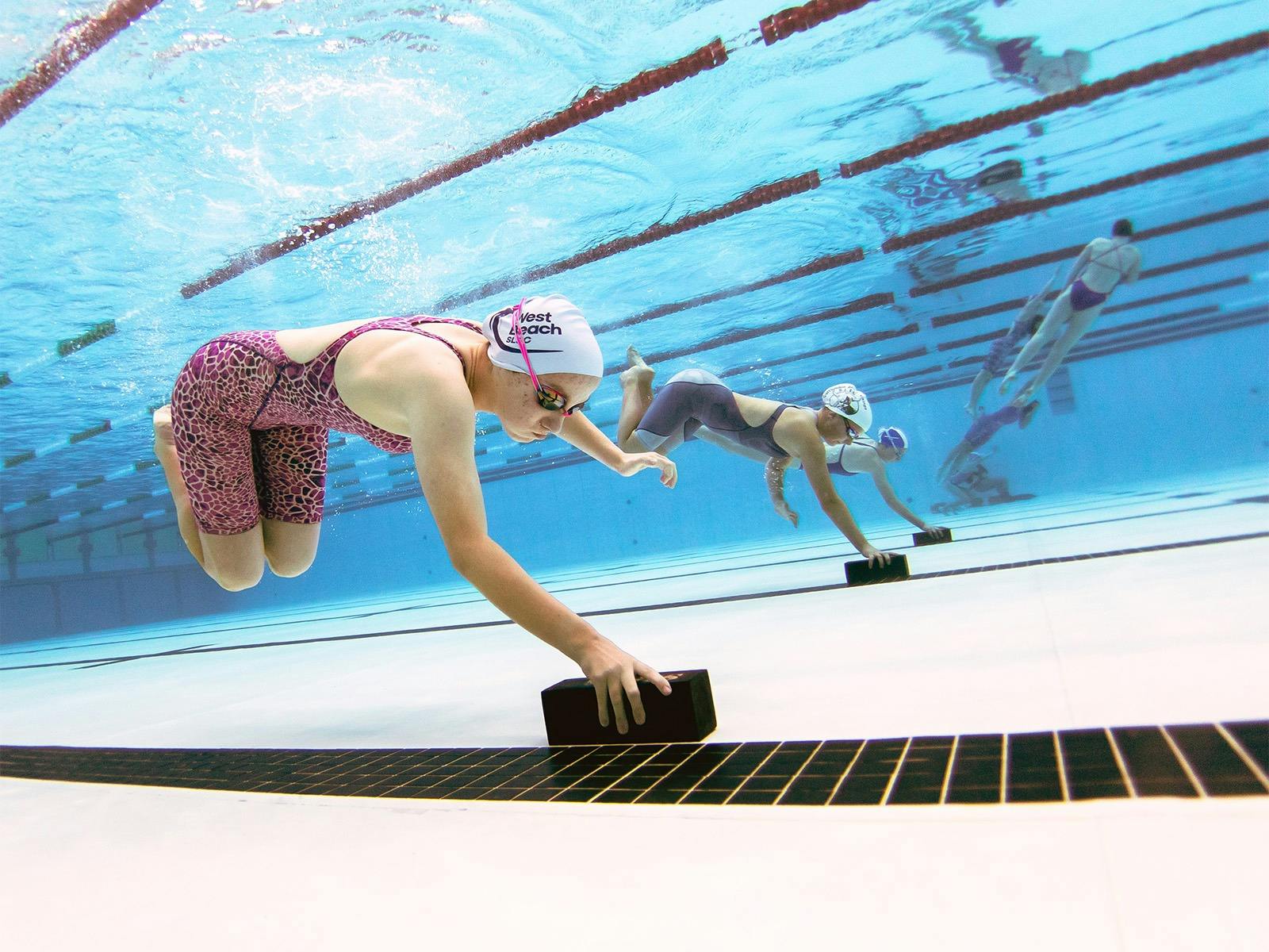 Youth competitors picking up weighted bricks from the pool floor during a race