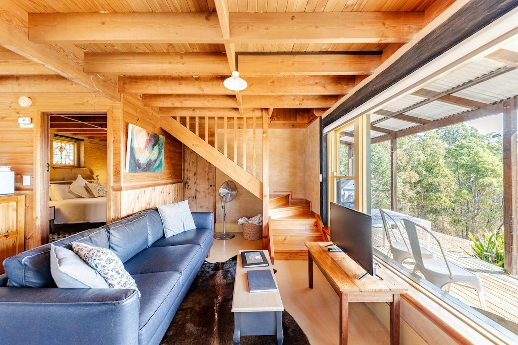 A black sofa faces a large picture window. Forest is visible through the glass.