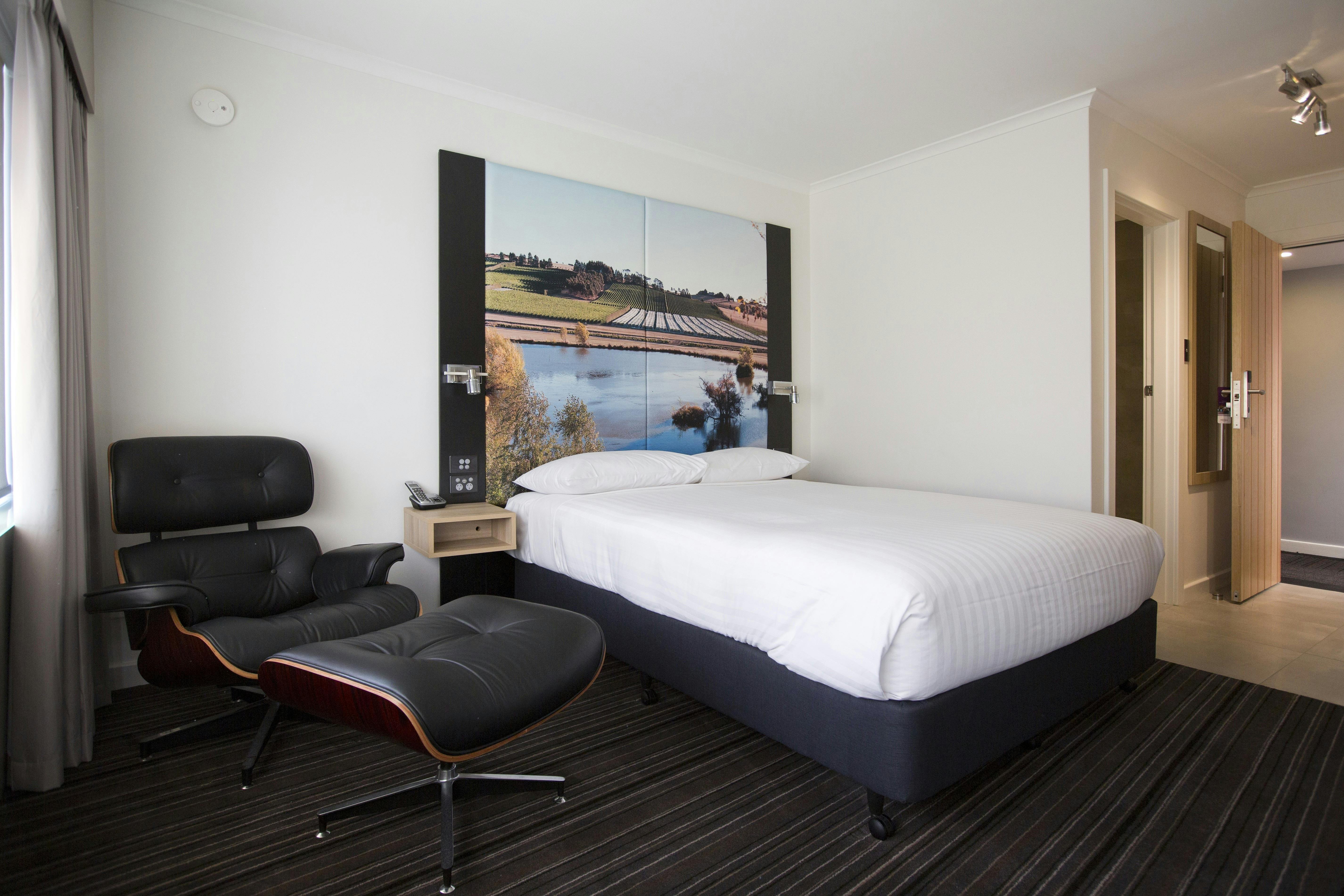 Guest accommodation room, with queen bed, chair and footstool.
