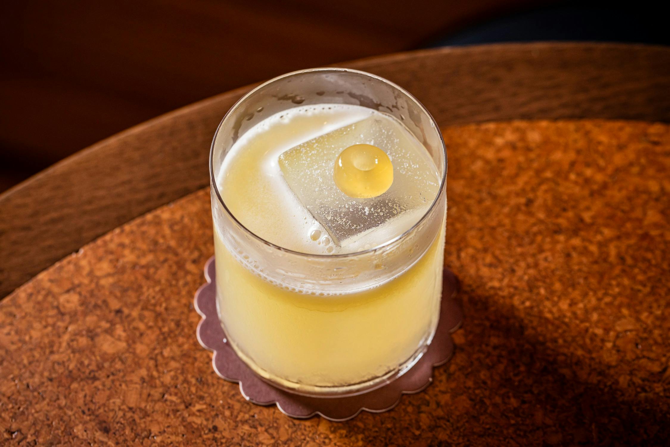 Yellow hued cocktail with jelly ring garnish on top of an ice cube