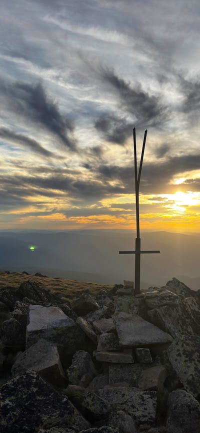 A hiker standing at the summit of a mountain with the sun setting behind them.