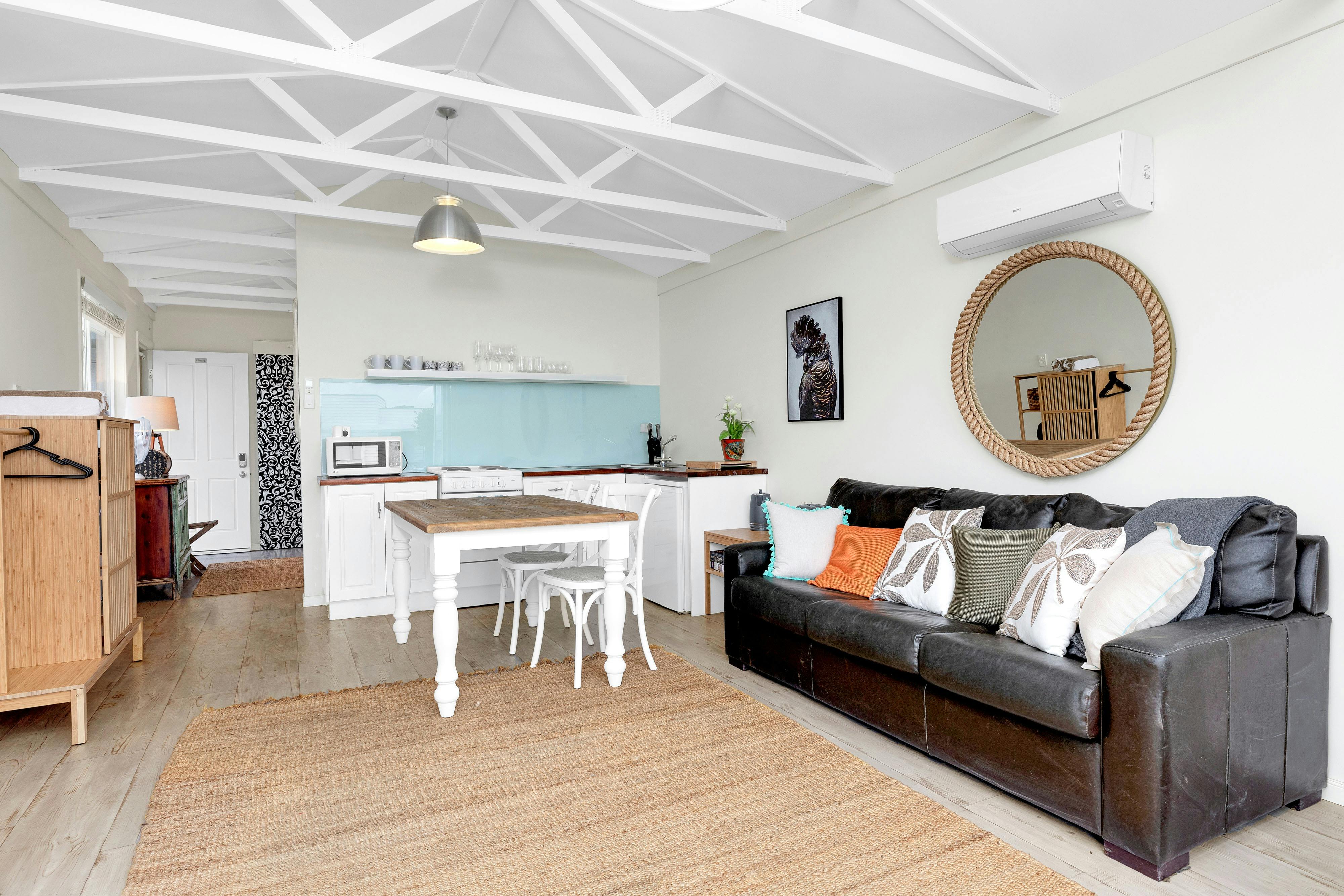 Interieor with black leather lounge, dining table, kitchen, wall mirror and exposed white timber bea