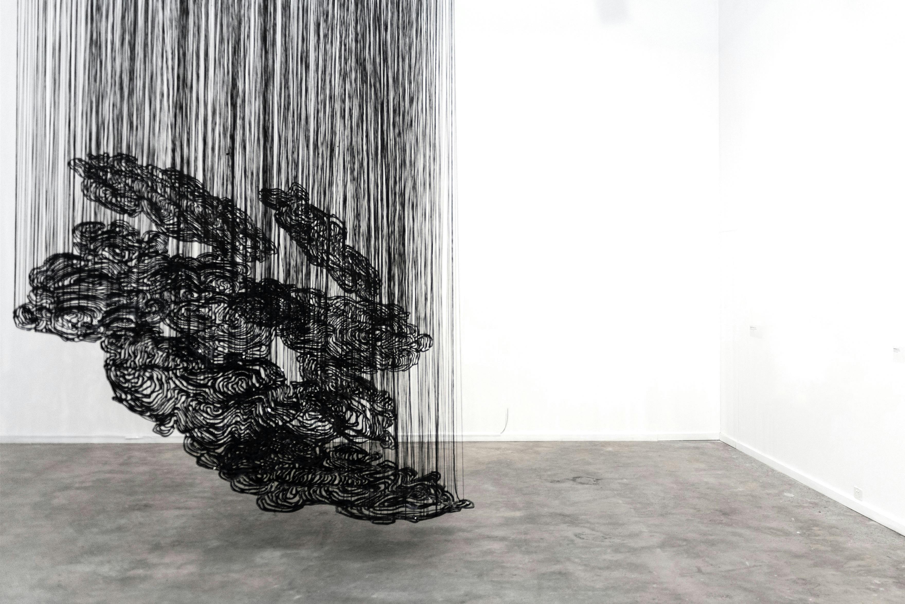 A black  artwork installation suspended from the ceiling of an art gallery.