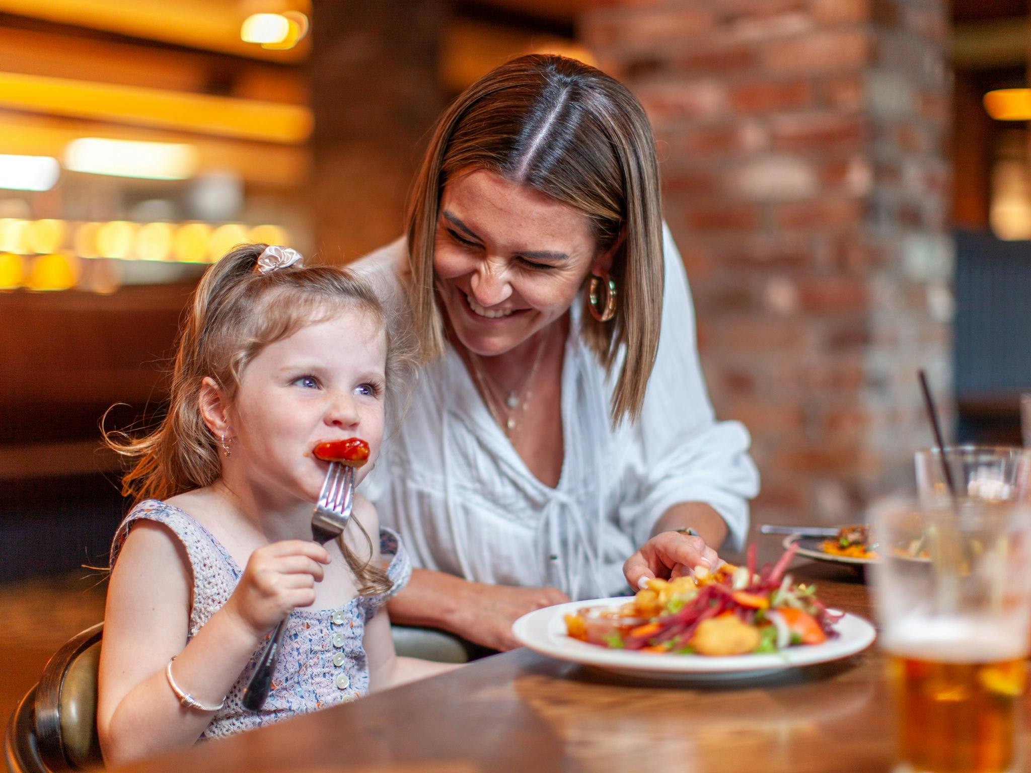 A child and a woman sitting next to one another at Harrigan's Hunter Valley laughing and eating