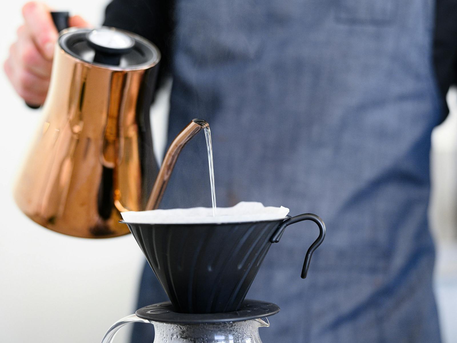 Barista pouring water over a v60 filter coffee with a copper kettle.