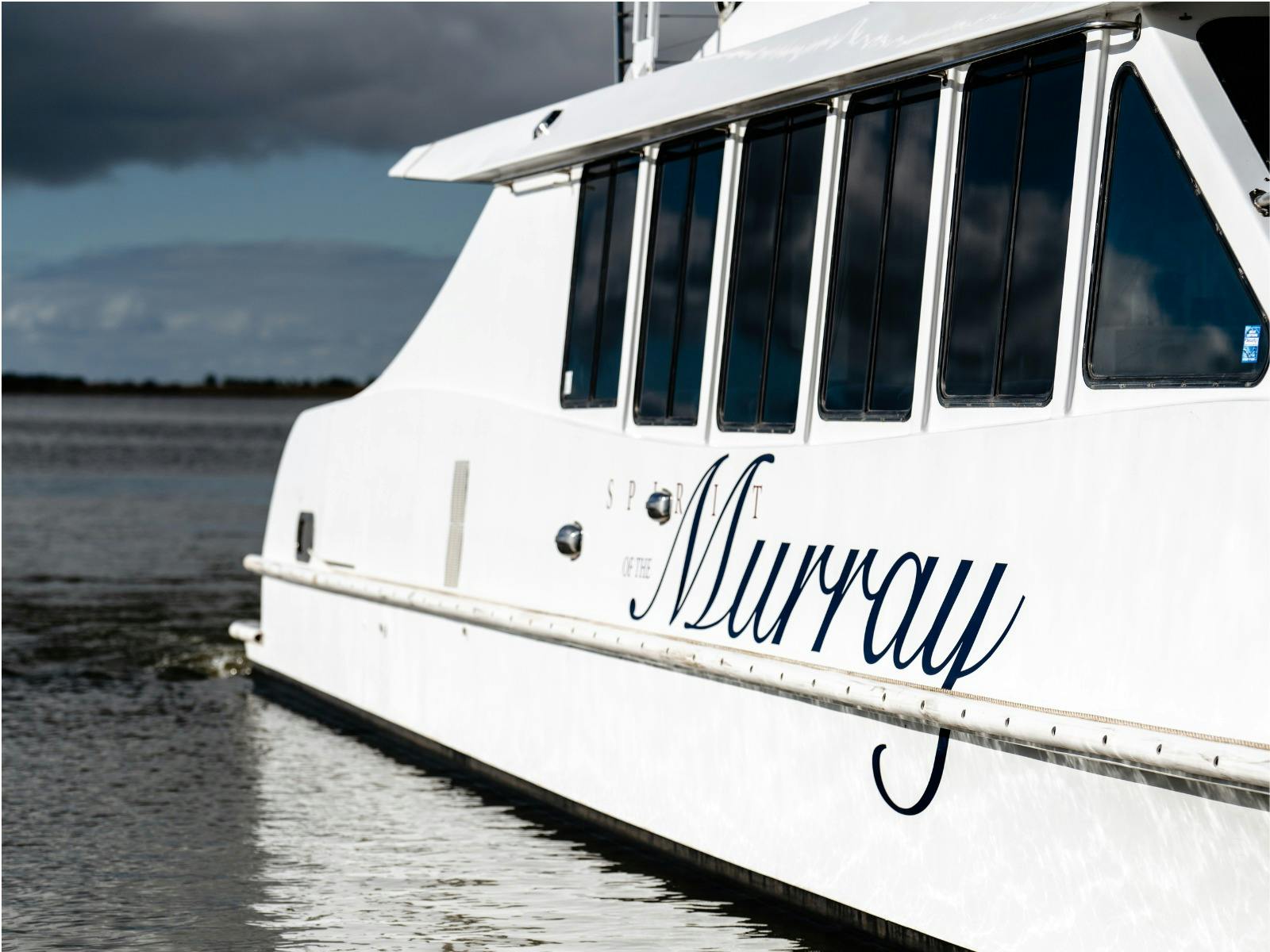 The "Spirit of the Murray" boat on water, with reflections and a cloudy sky in the background