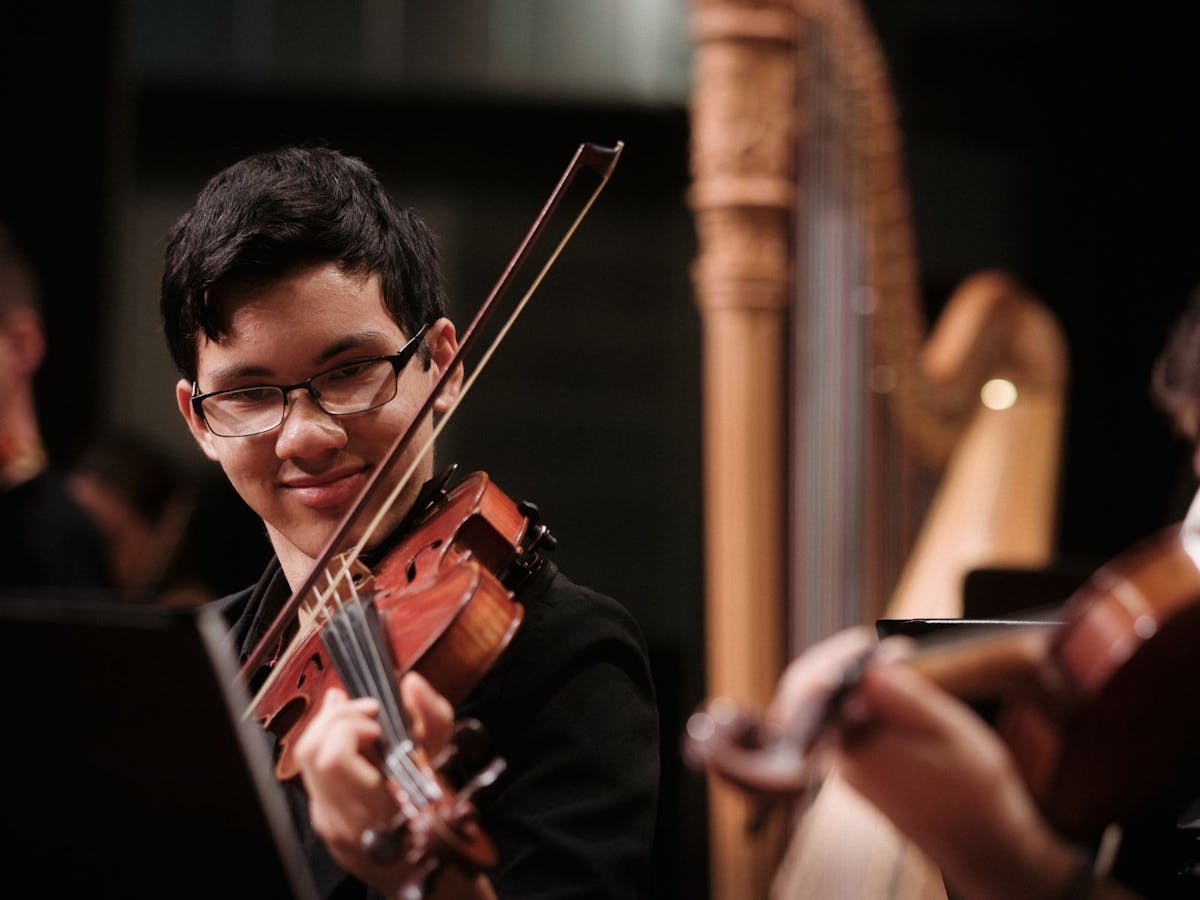 A young musician plays violin as part of an orchestra