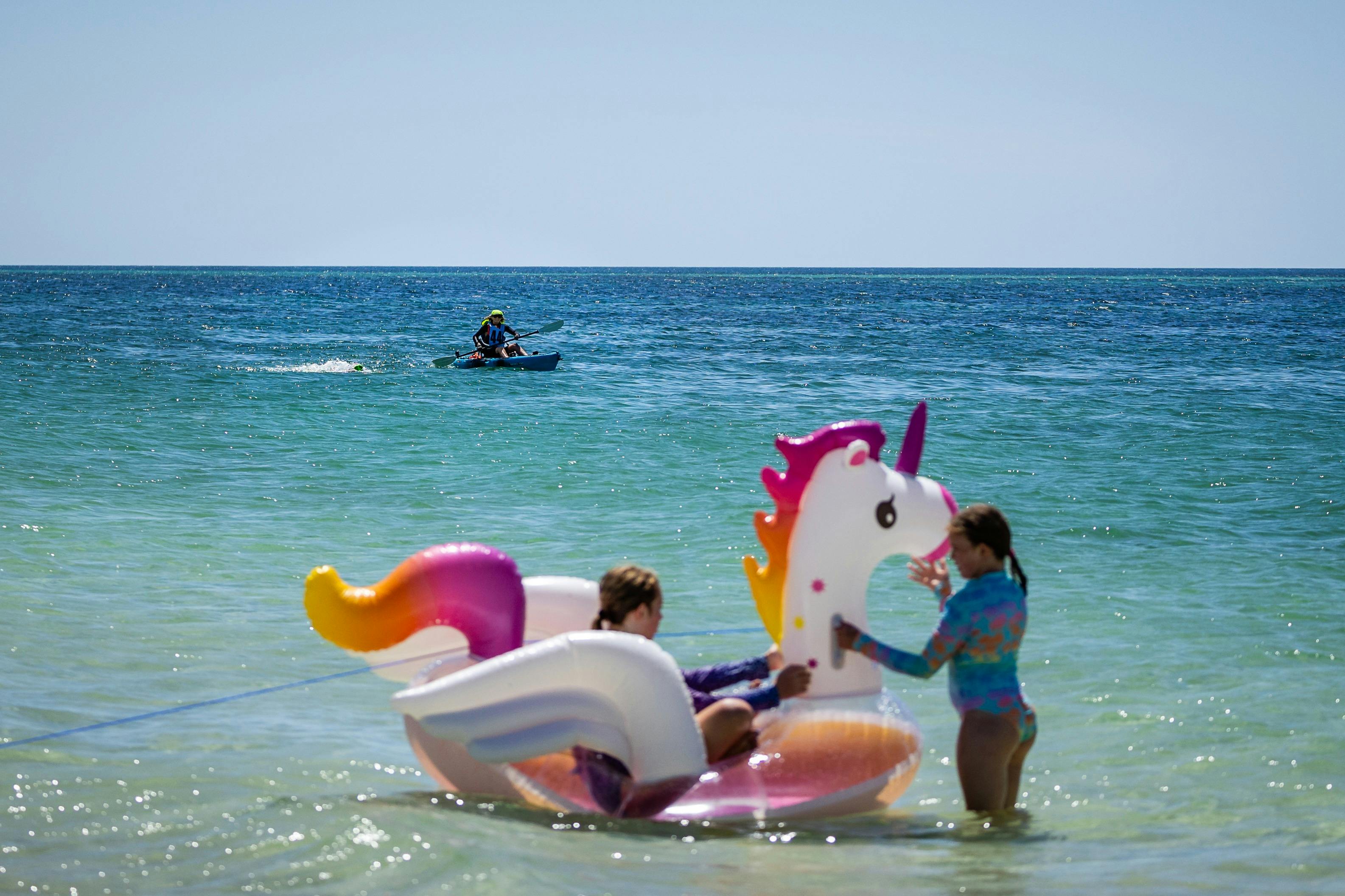 children enjoy the beach party as a swimmer passes by in the background.
