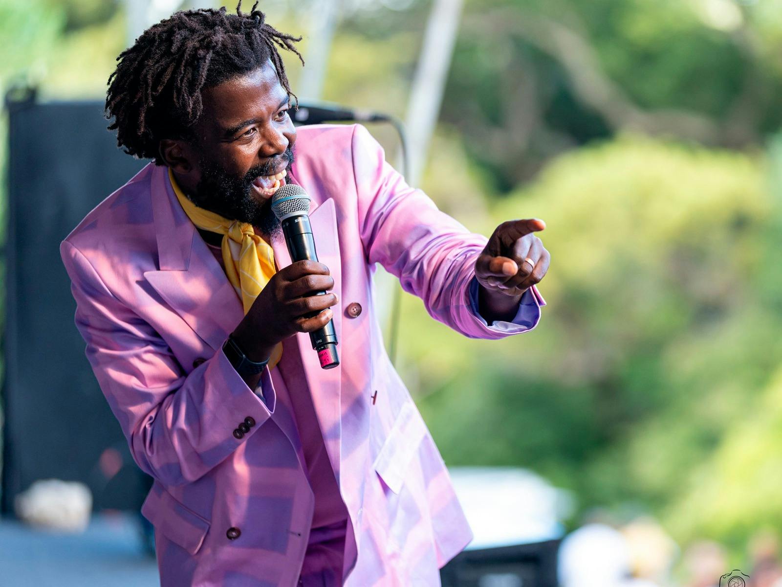 An artist performs on stage wearing a purple suit and singing