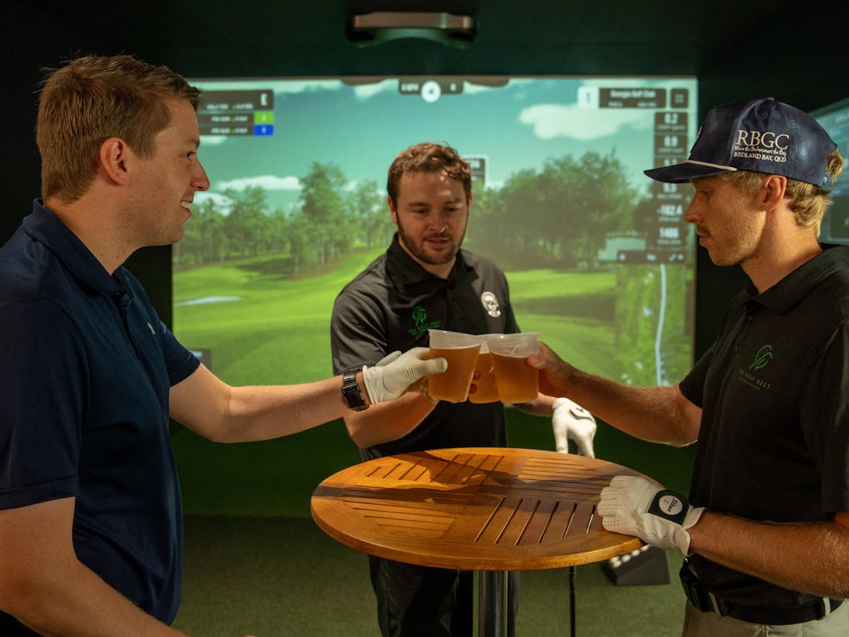 3 men enjoy beers and cheers to a great round in front of the golf simulator