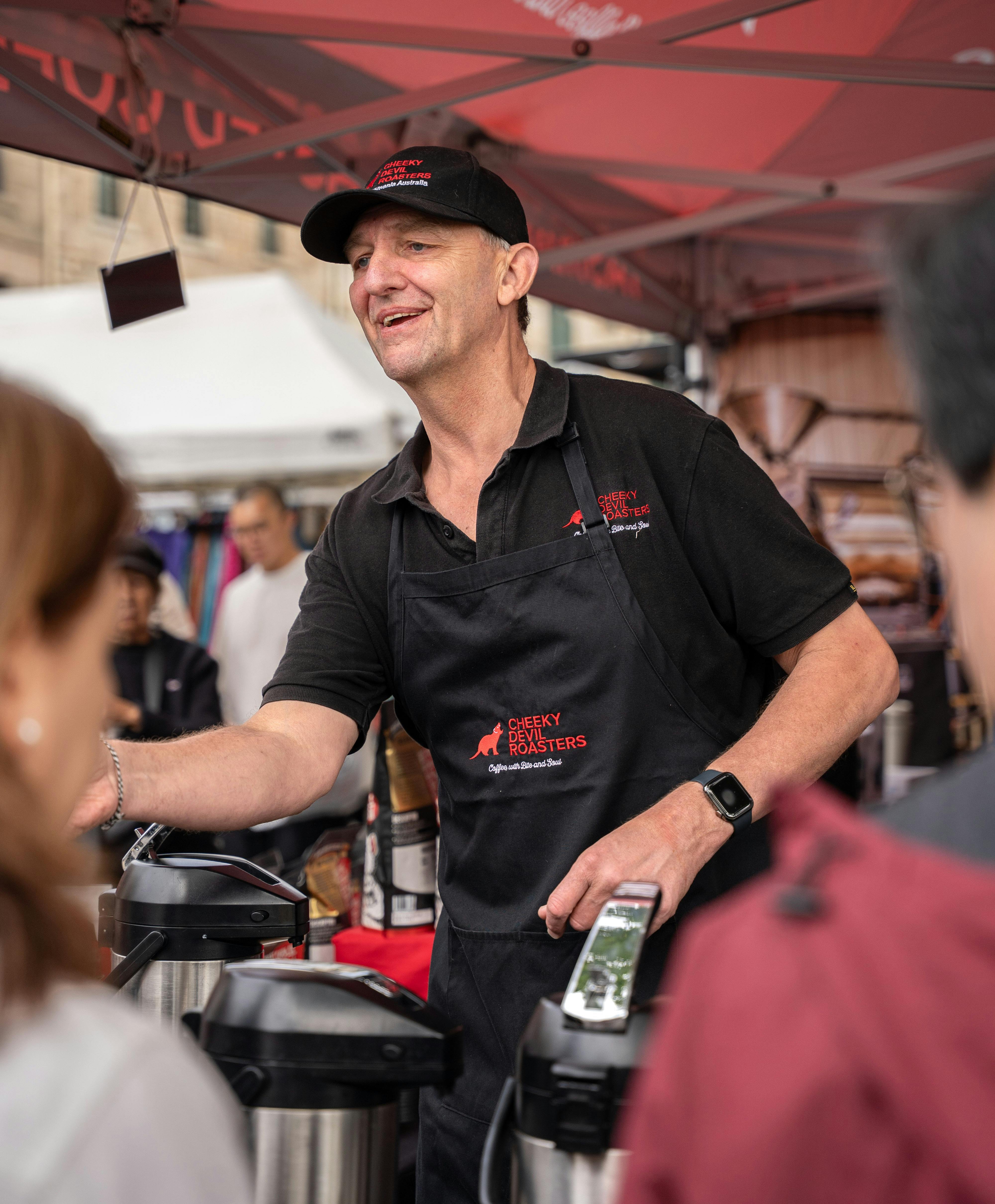 Cheeky Devil team member serving coffee to a customer at Salamanca Market