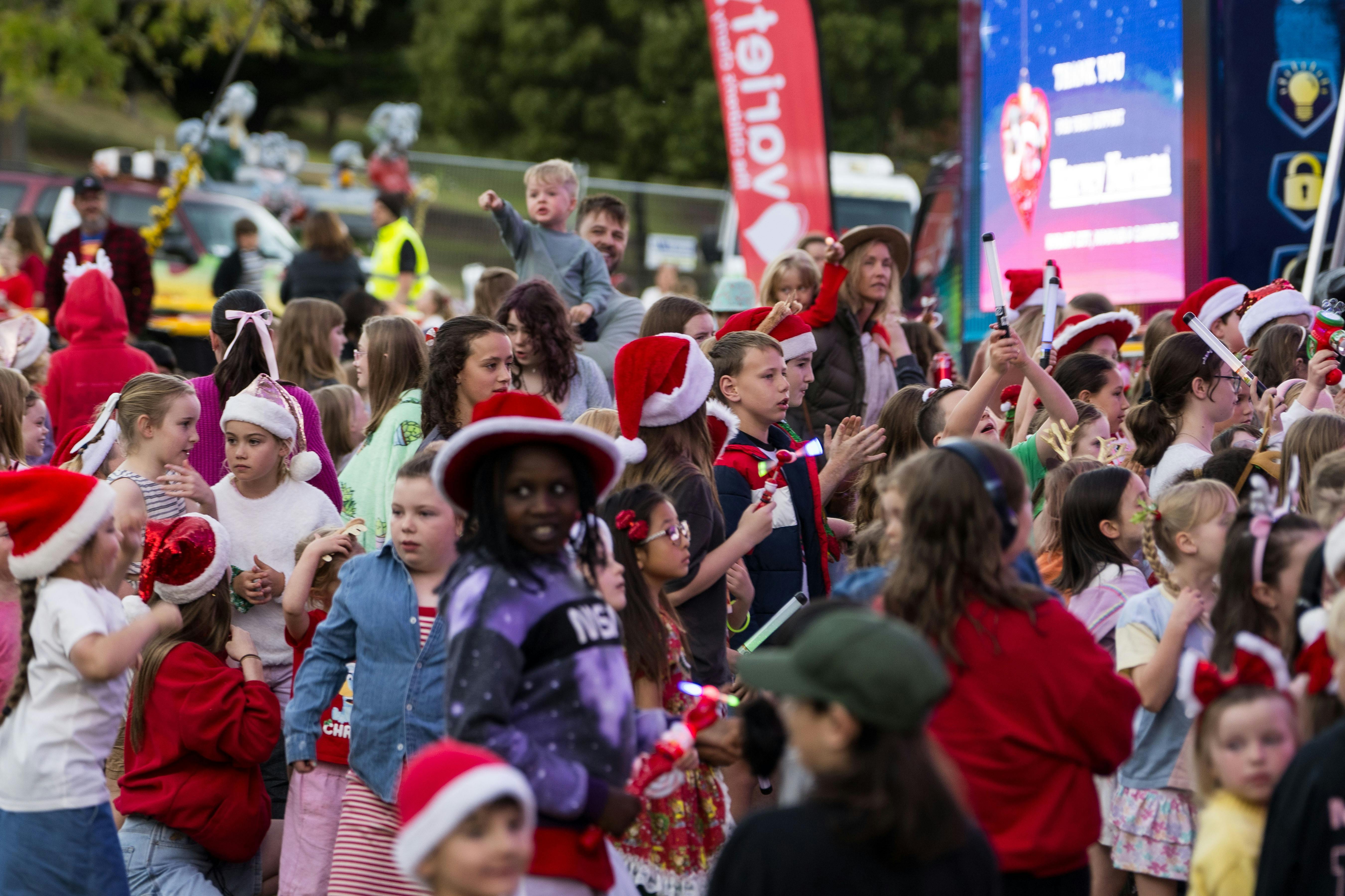 crowd of Christmas themed kids singing along to Christmas carols at the  Carols by Candlelight