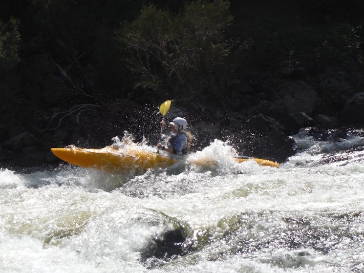 A kayak is launching itself out of the water on top of a wave in one of the many rapids on the Snowy