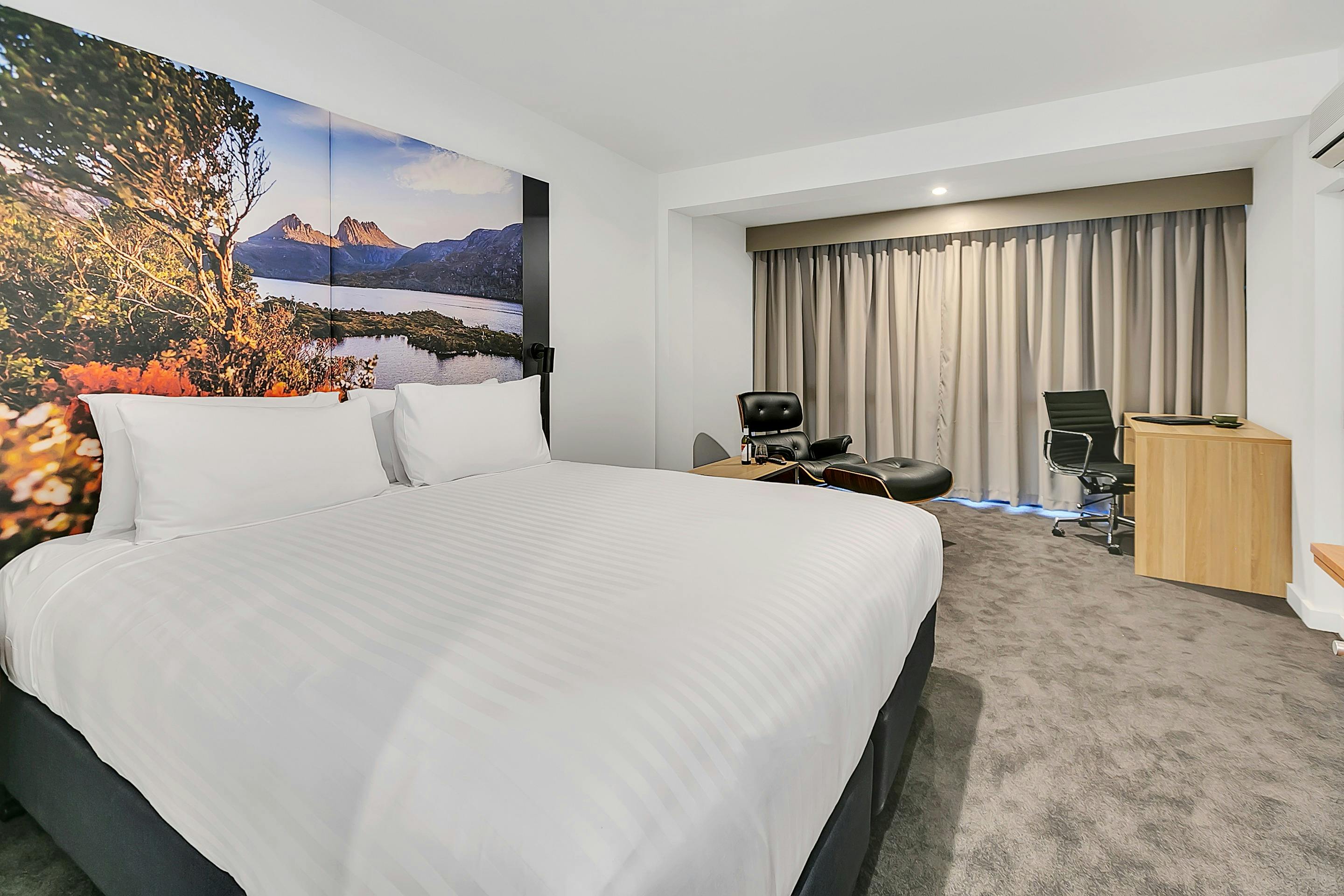 Guest accommodation room, with king bed, spacious with chair/footstool, large window with curtain.