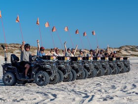 Group of people sitting on quad bikes while parked on the beach
