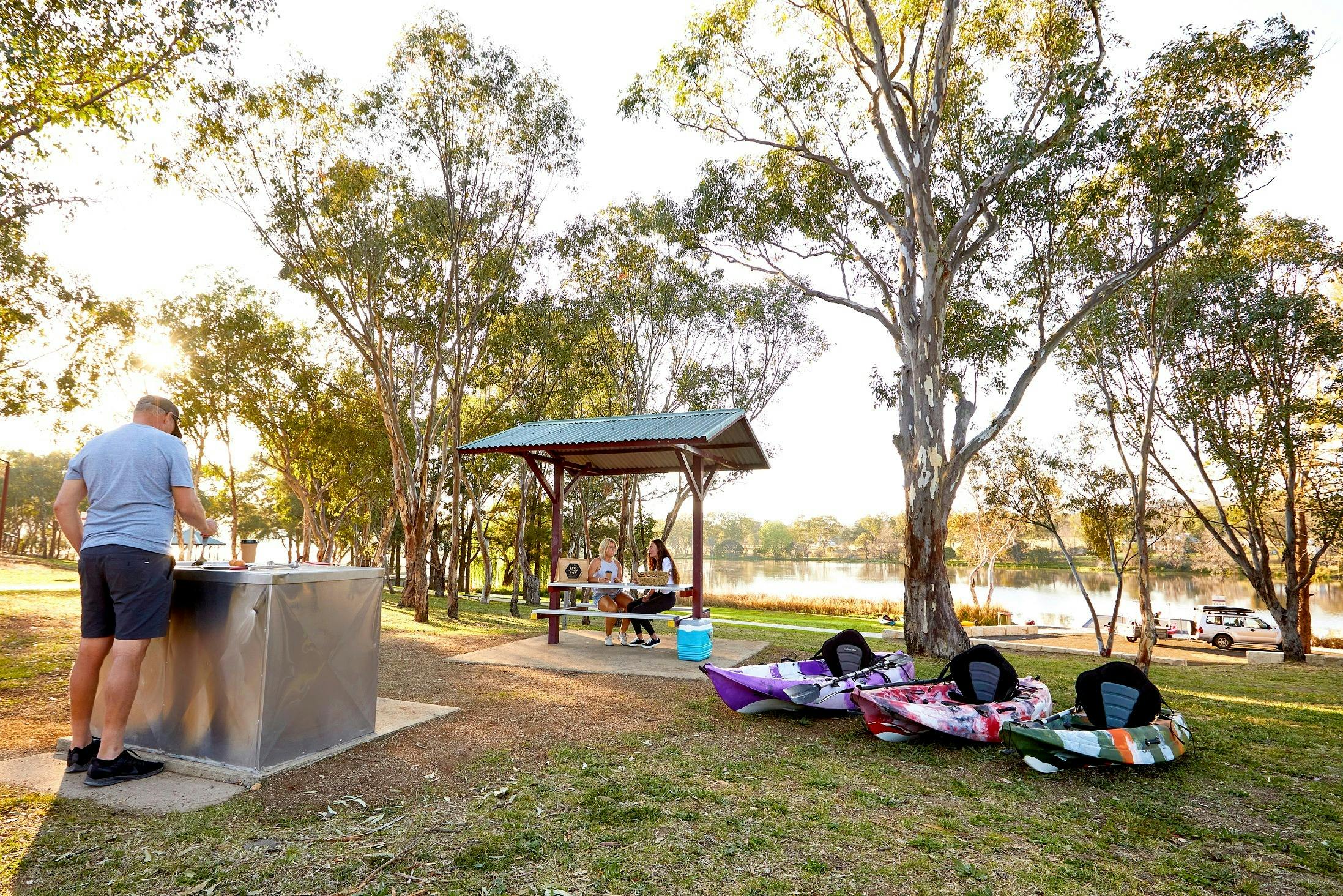 Lake Inverell Picnic area. Man at BBQ on left, two ladies sitting at Picnic Table on right.