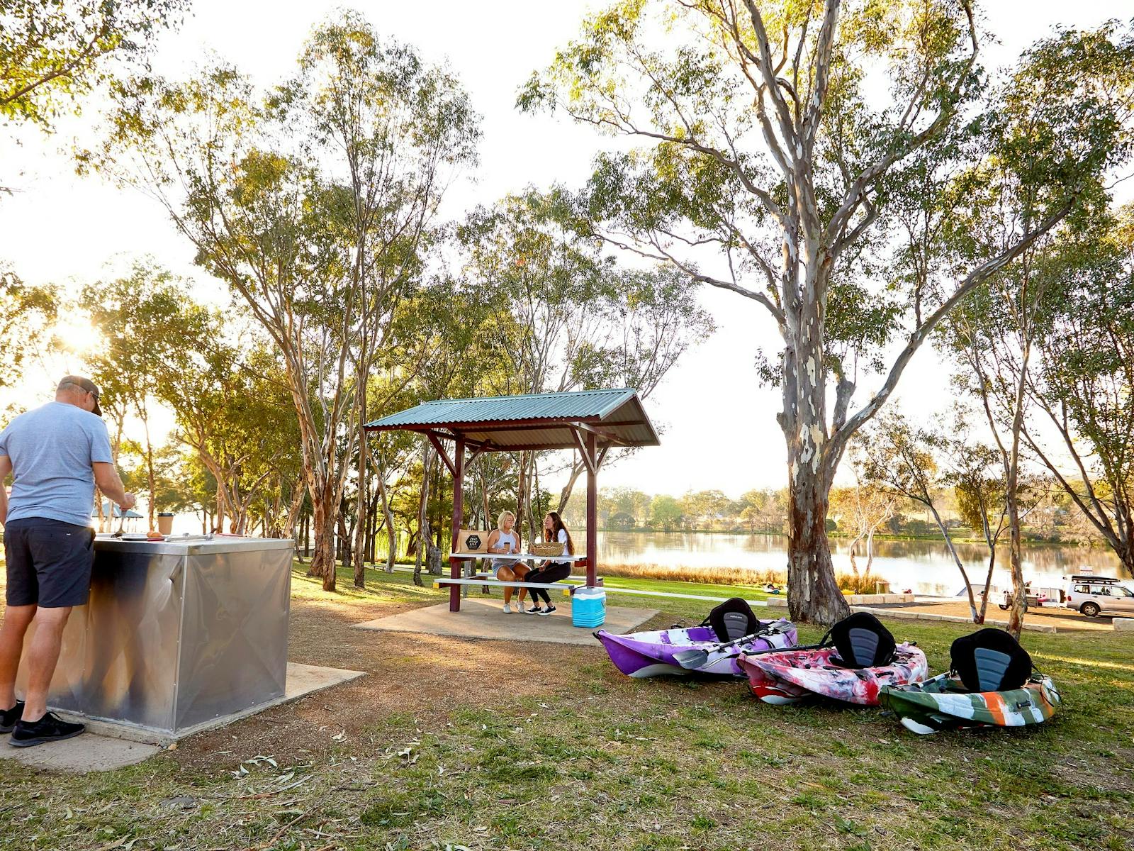 Lake Inverell Picnic area. Man at BBQ on left, two ladies sitting at Picnic Table on right.