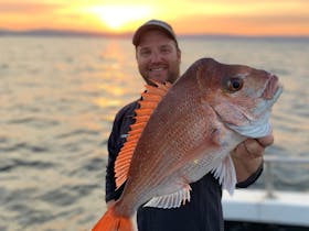 Man holding a snapper against the sunrise