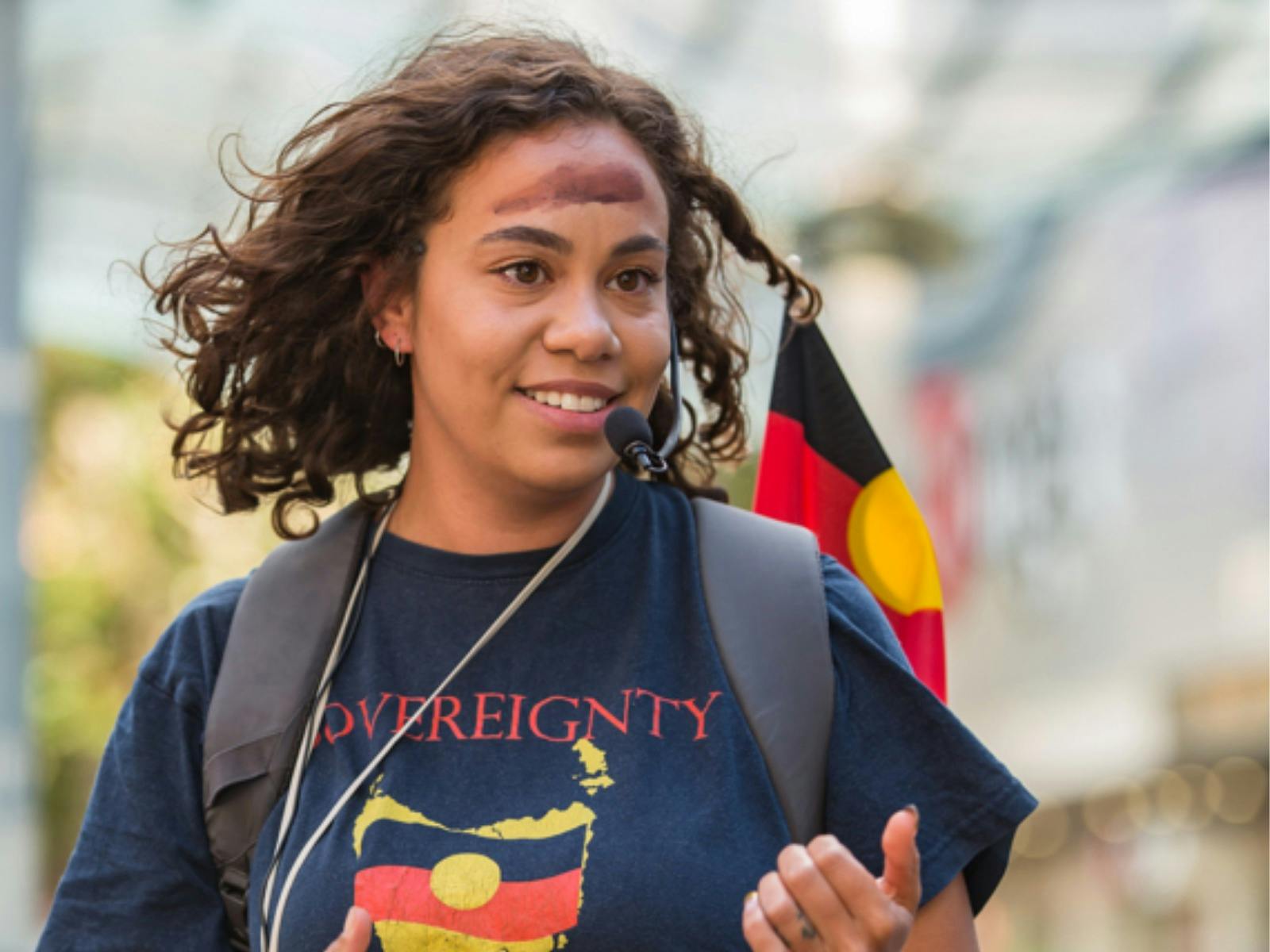 Woman named Nunami stands wearing black T-shirt with text "sovereignty" & map of Tasmania