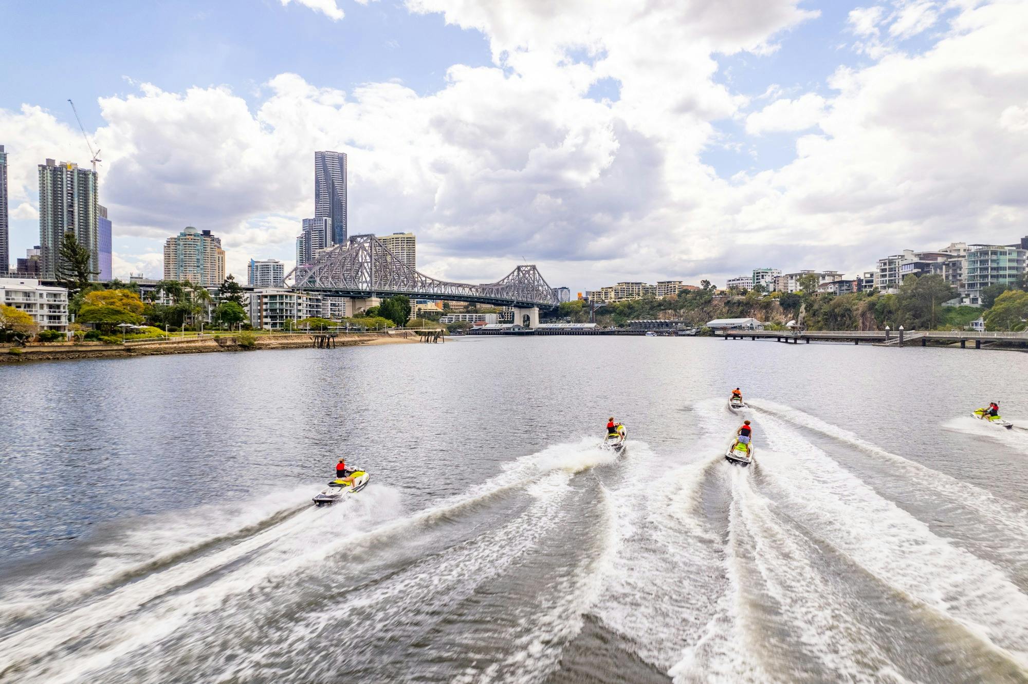 Aerial view of group of people on jet skis cruising through the Brisbane River with Brisbane City sk