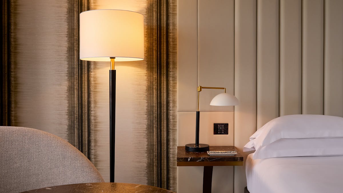 Warm lighting, marble side table and padded wall panels beside a hotel bed