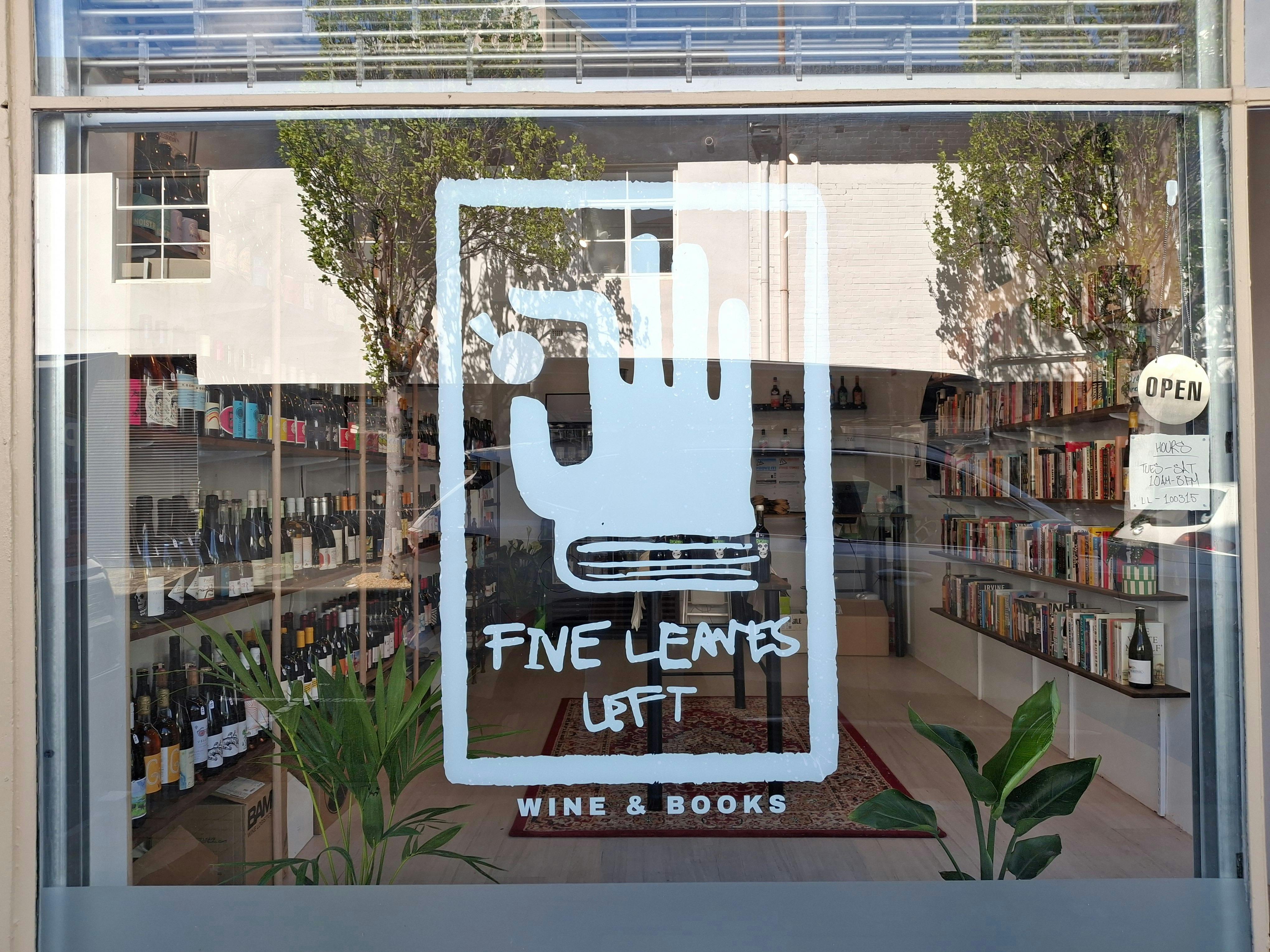Window shop front featuring brand logo signage with natural wines and books in the background