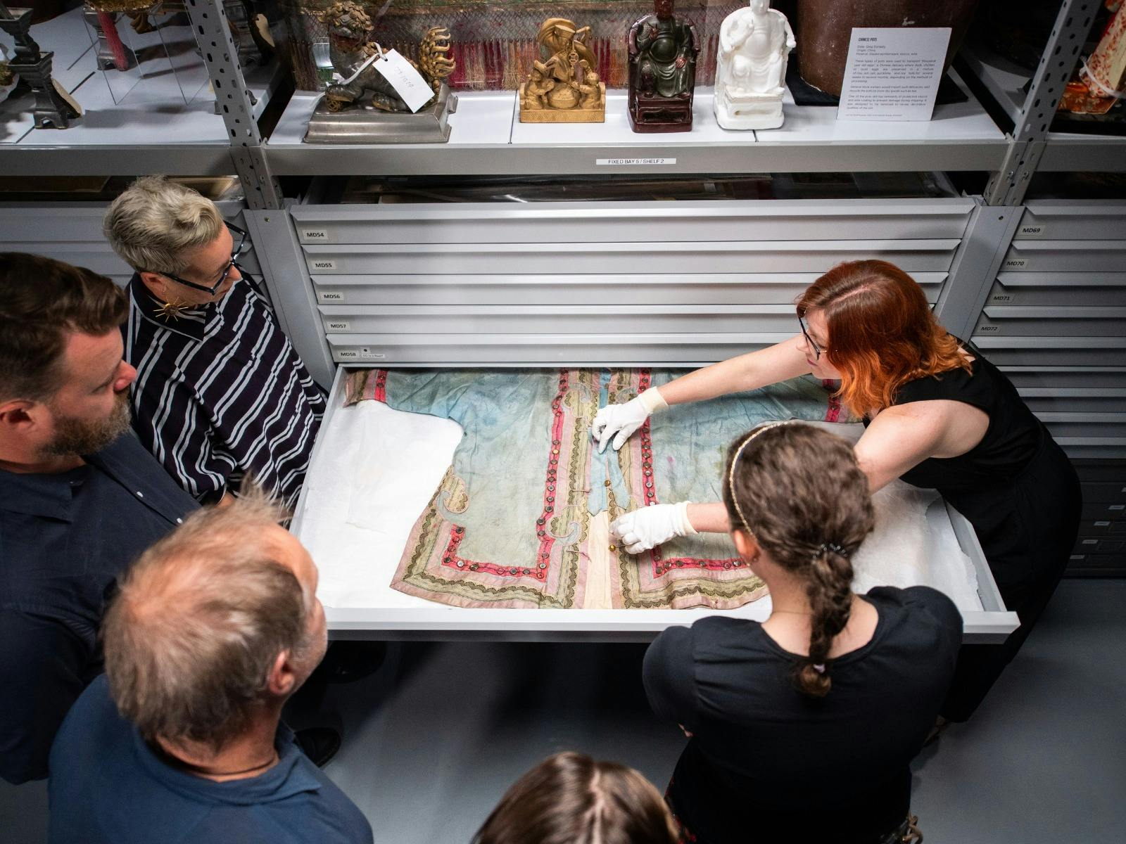 Curator showing Chinese garment in drawer to tour group