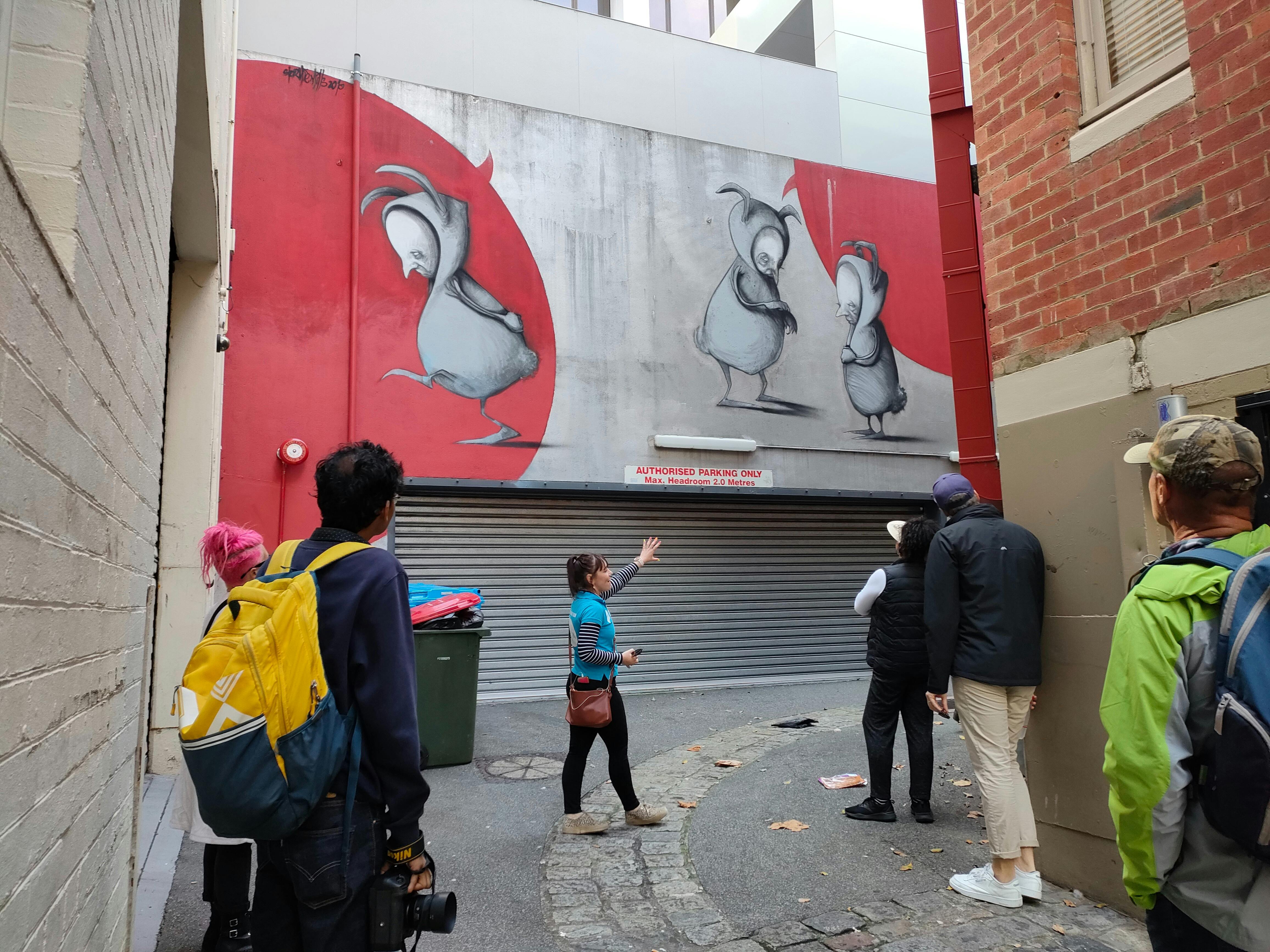 a tour guide pointing out a mural to a group of guests in a laneway