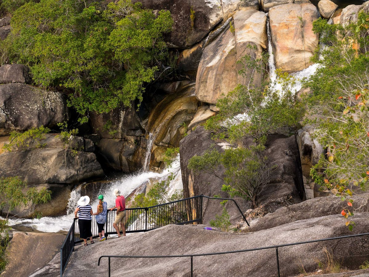 Three people standing at granite rock lookout watching a waterfall.