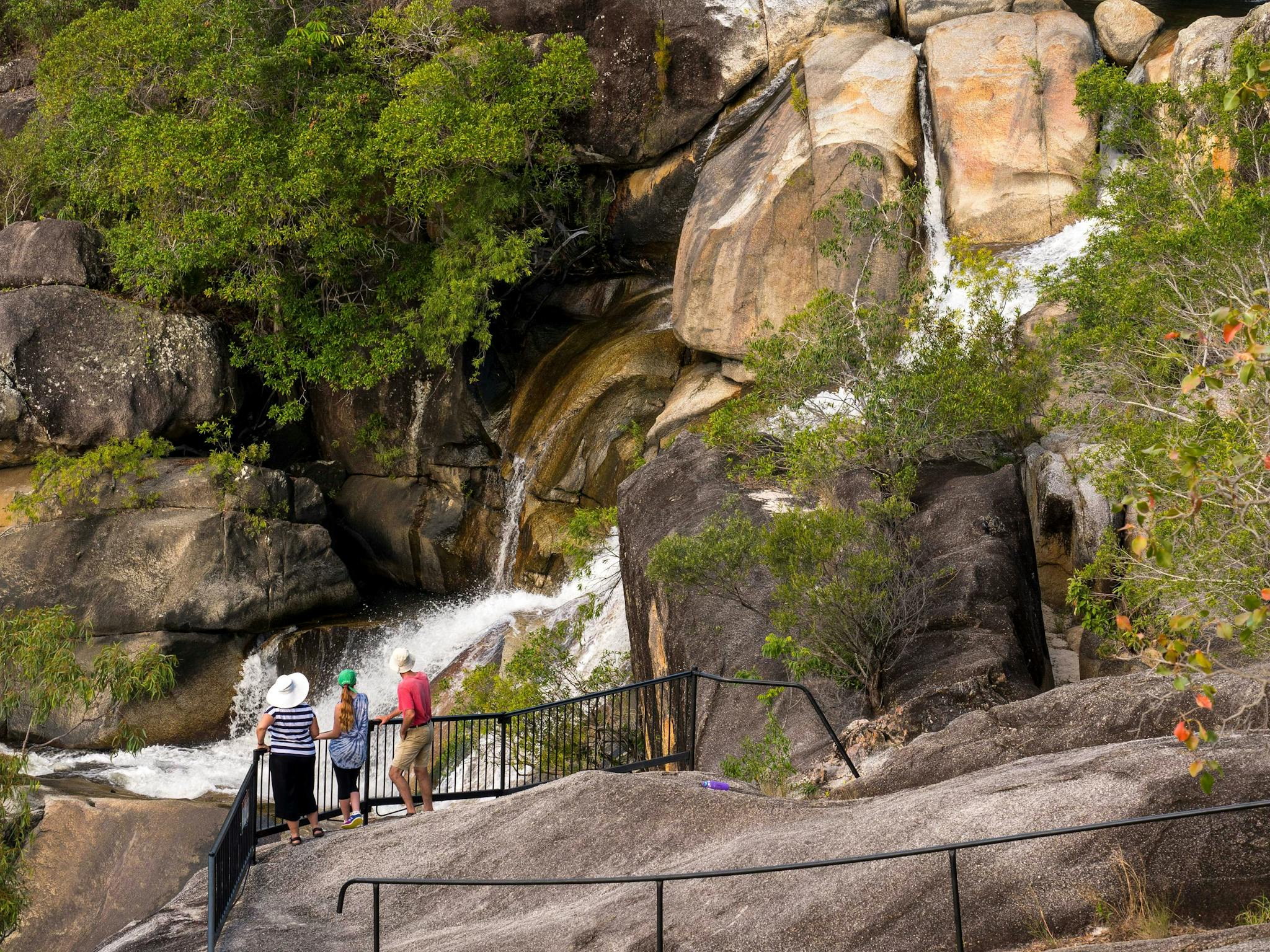 Three people standing at granite rock lookout watching a waterfall. Three people standing at granite rock lookout watching a waterfall.