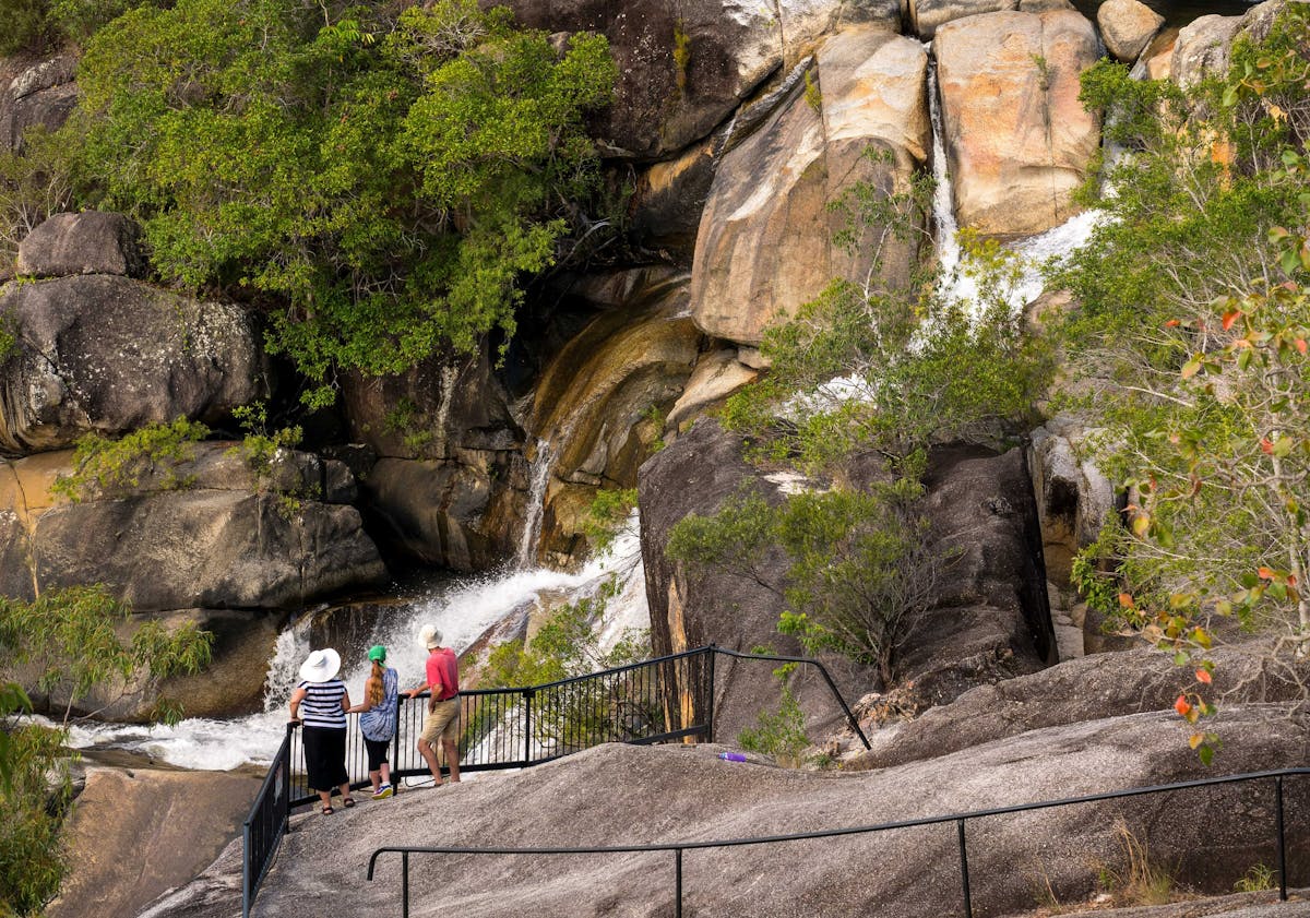 Three people standing at granite rock lookout watching a waterfall.